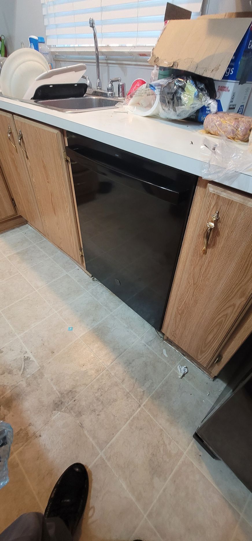 Kitchen counter with sink, black dishwasher, and wicker cabinet doors, with dishes and items on the countertop