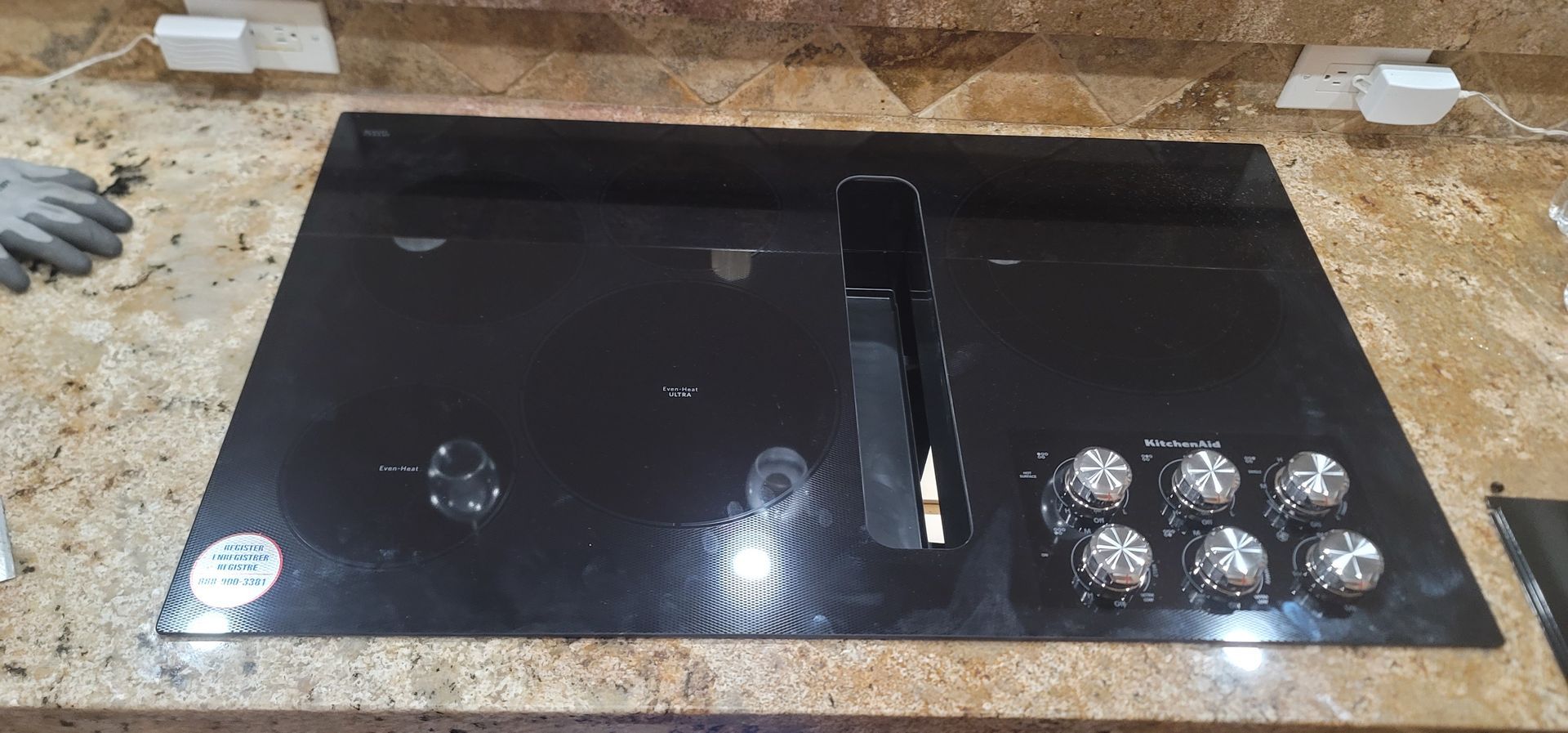 Black glass cooktop with burners, knobs, and a central vent on a dusty work surface