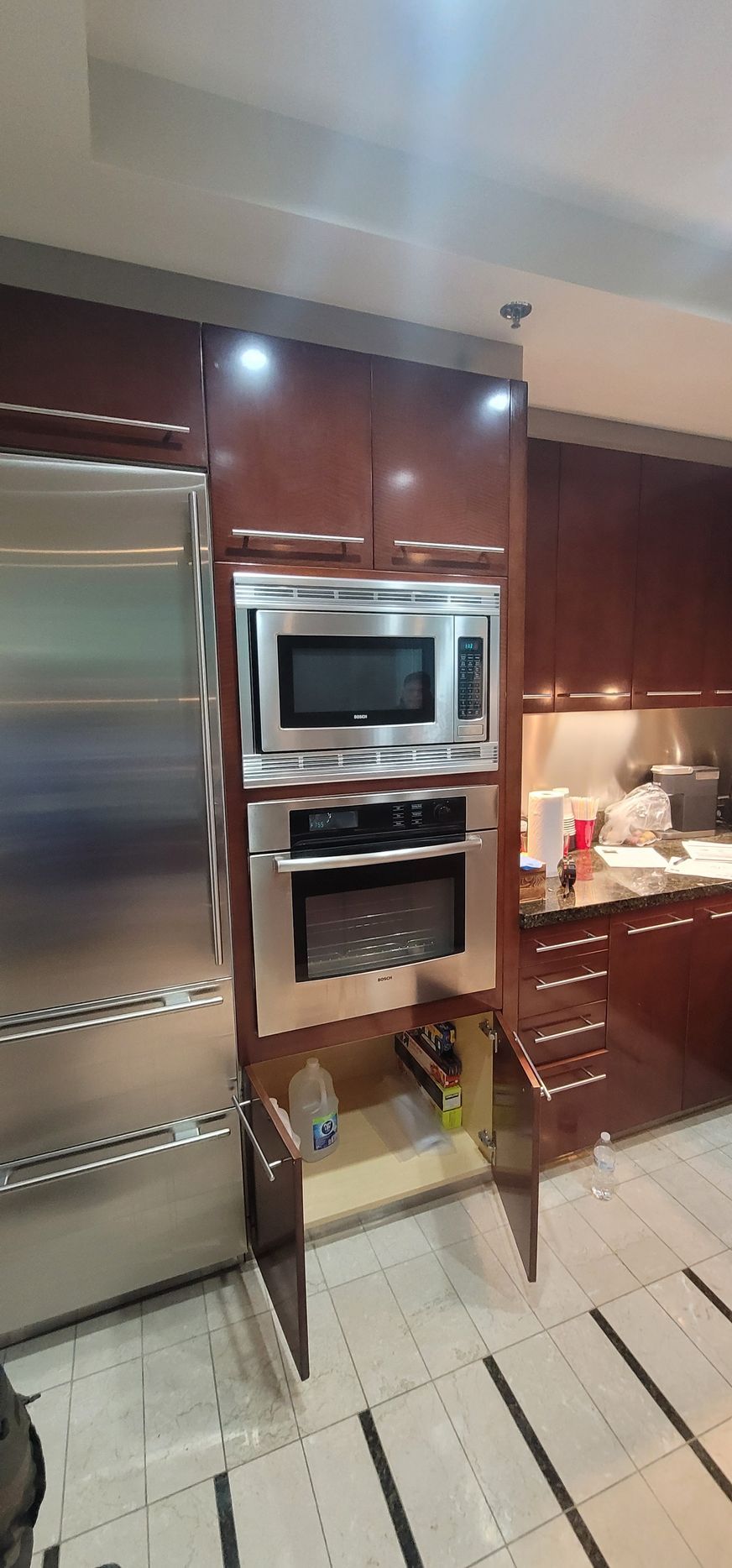 Kitchen with stainless steel fridge, built-in microwave and oven, dark wood cabinets, and tiled floor.