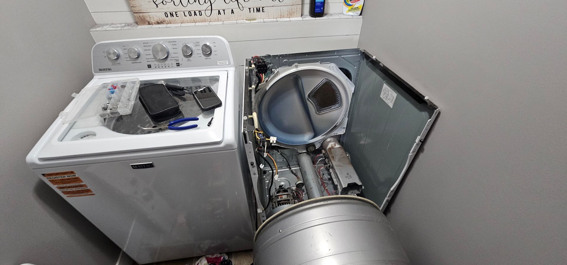 Open washing machine with clothes and a tilted dryer drum in a laundry room
