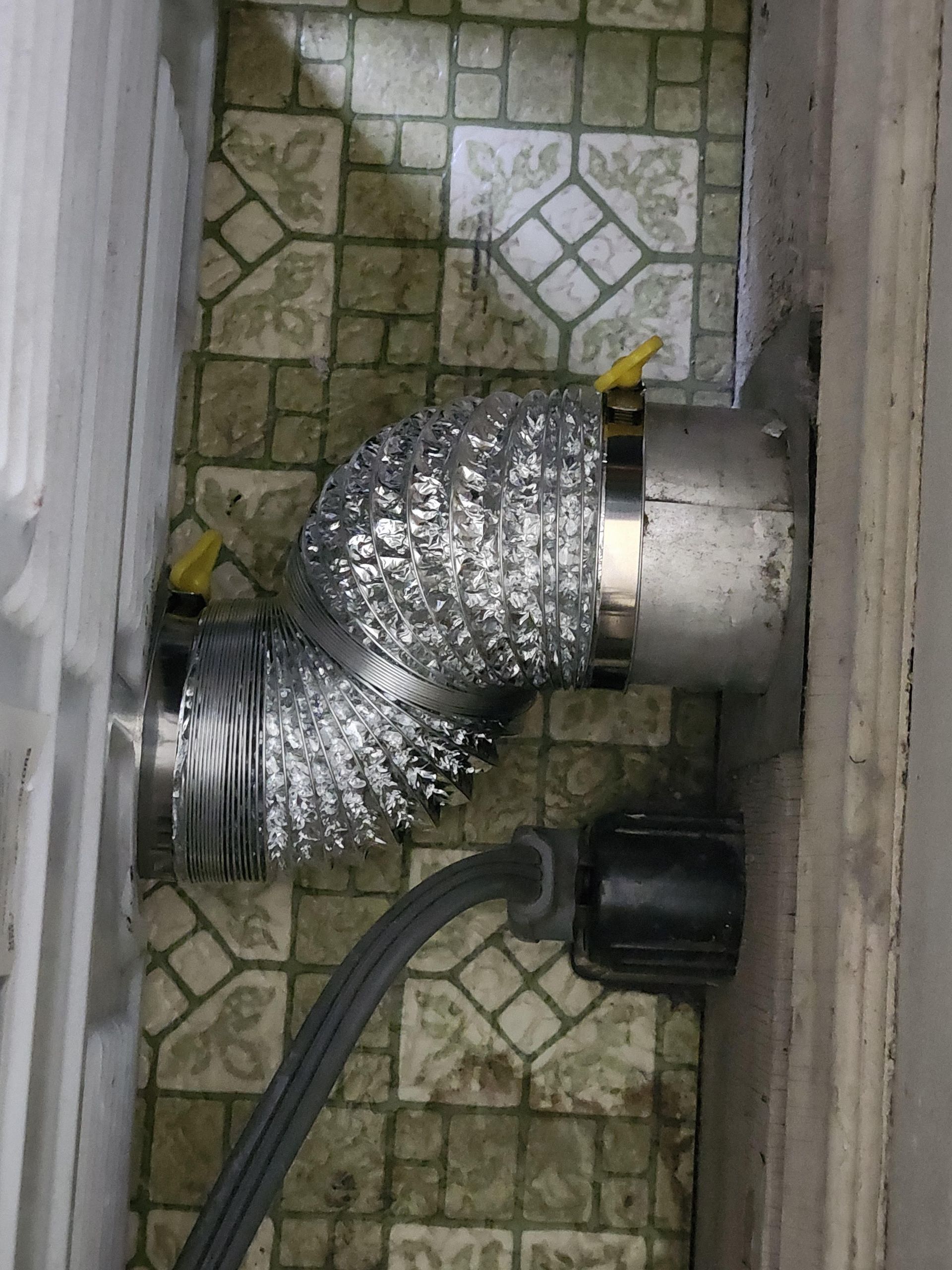 Foil-wrapped flexible duct connected to a wall vent on a tiled floor, with a black cable nearby