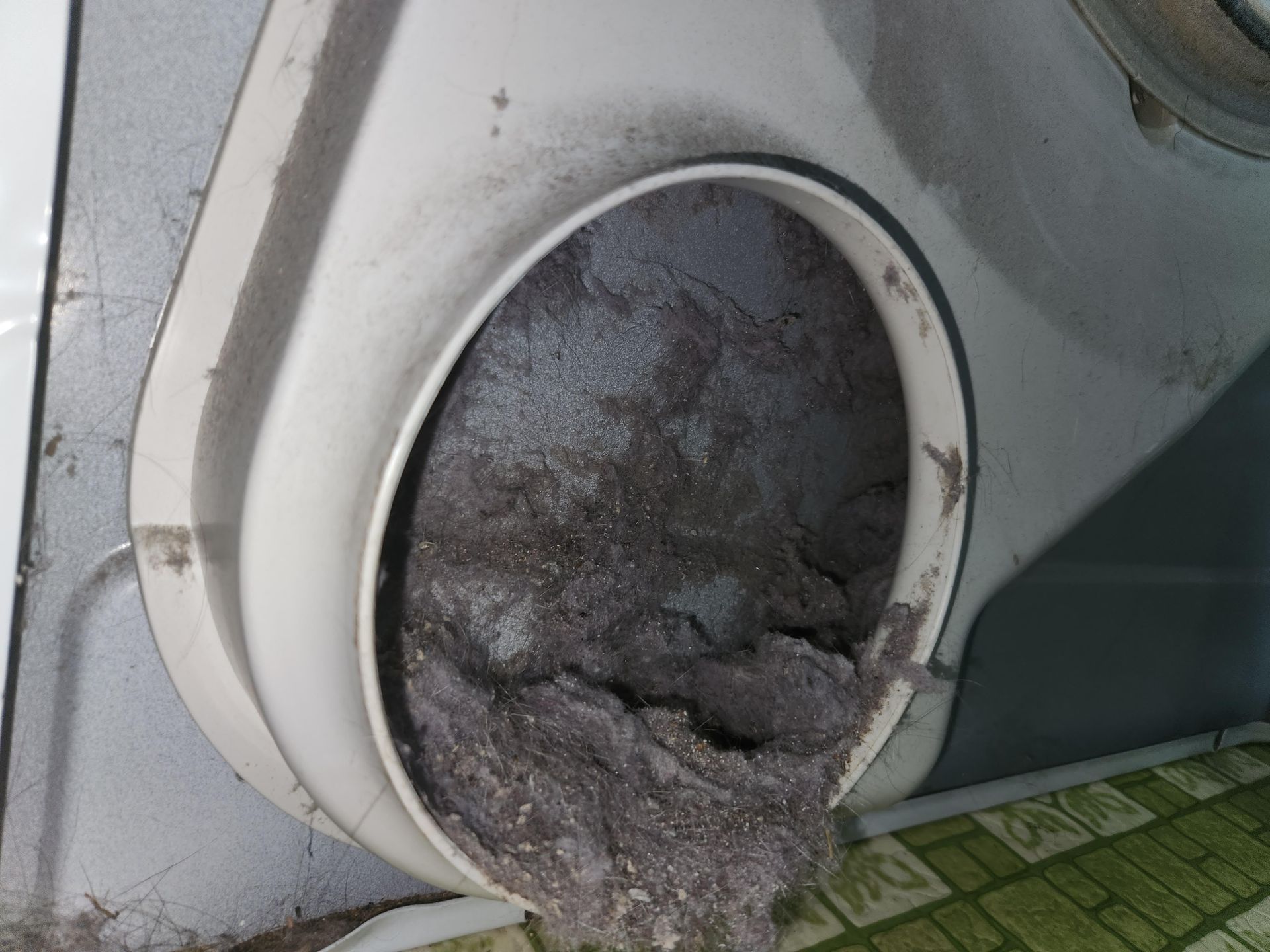 Dirty white circular vent opening clogged with gray debris or lint