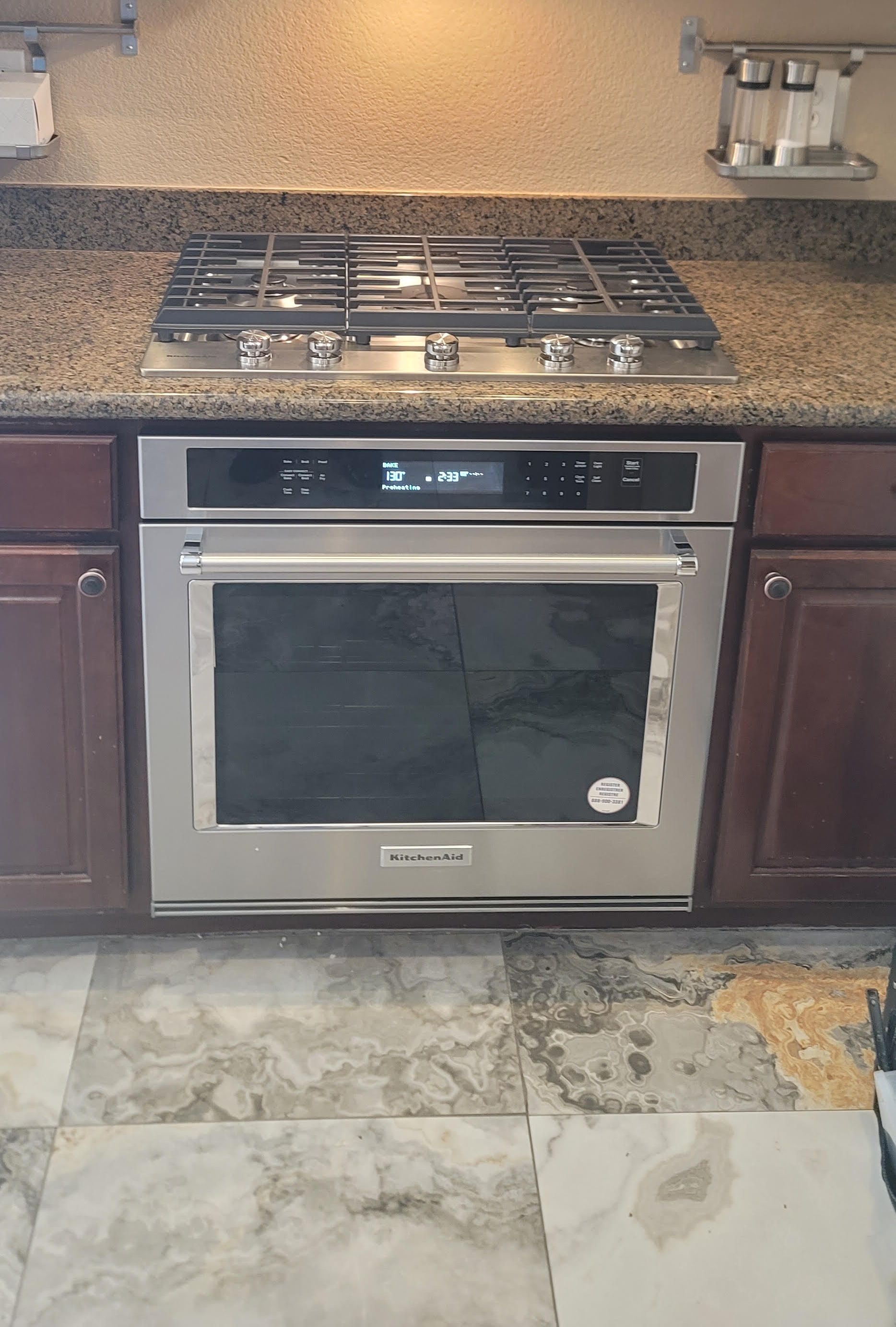 Kitchen stove and oven under granite countertop with dark wood cabinets and tiled floor.