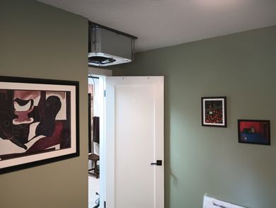Small room with sage-green walls, an open white door, and framed artwork hanging on the walls.