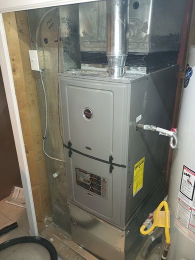 Gas furnace with silver vent pipe in a utility closet, surrounded by exposed framing and wiring.