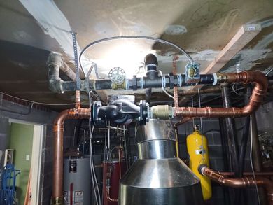 Basement mechanical room with copper pipes, ducts, and a large metal HVAC unit.