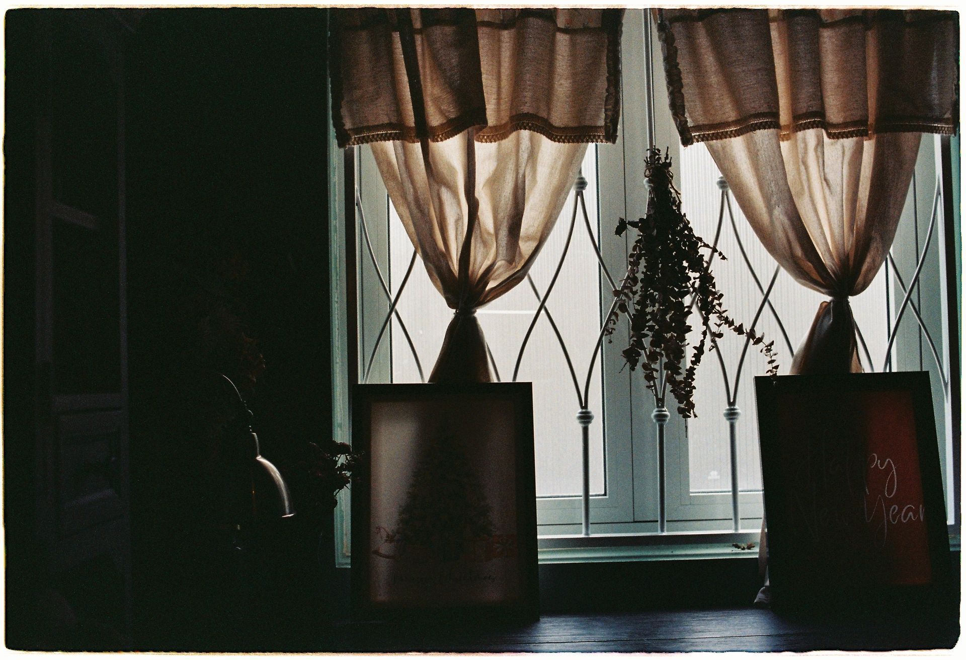 Dim room with two covered windows and sunlight filtering through sheer curtains.