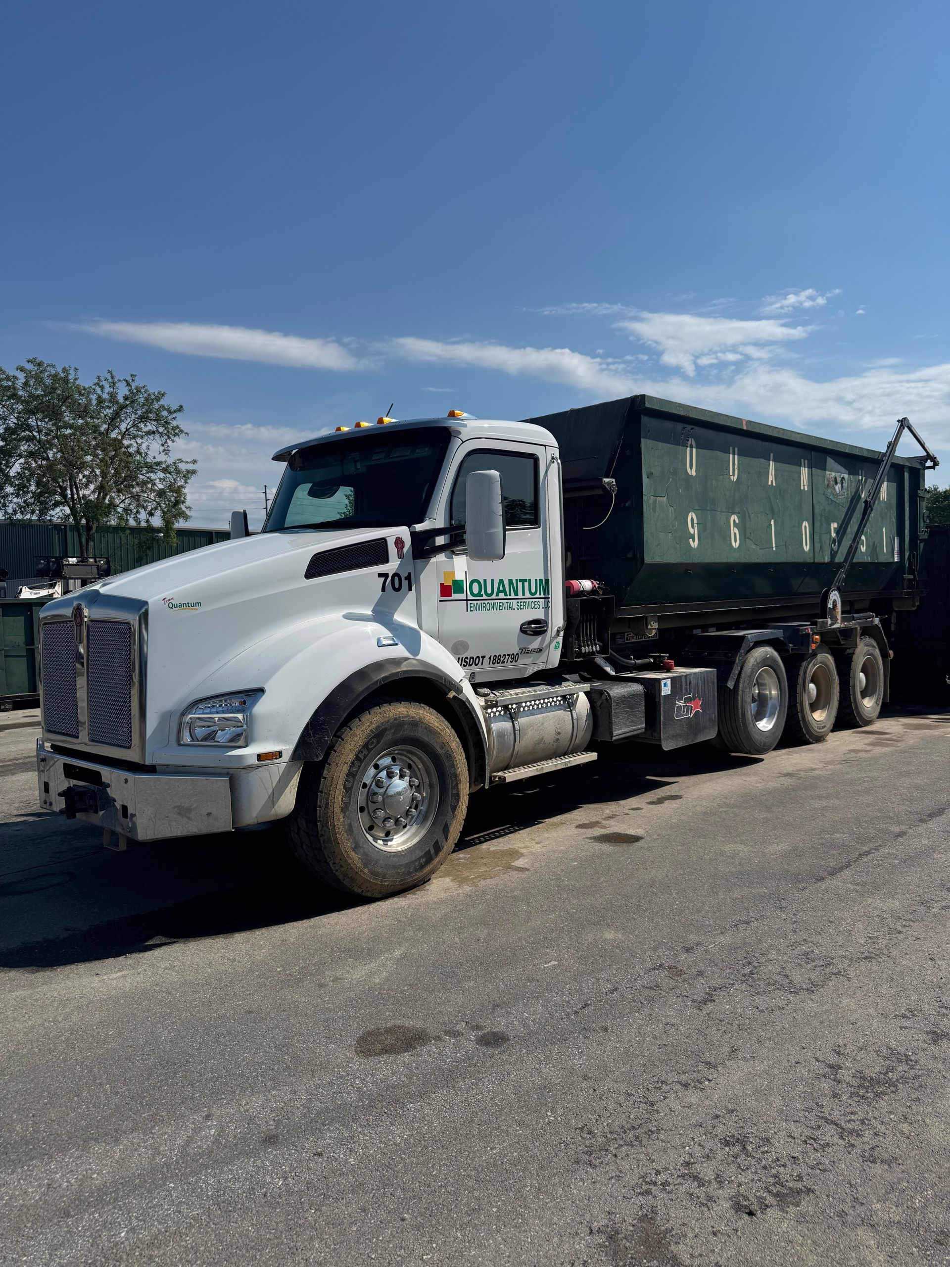 White dump truck parked on a sunny lot with a green trailer attached