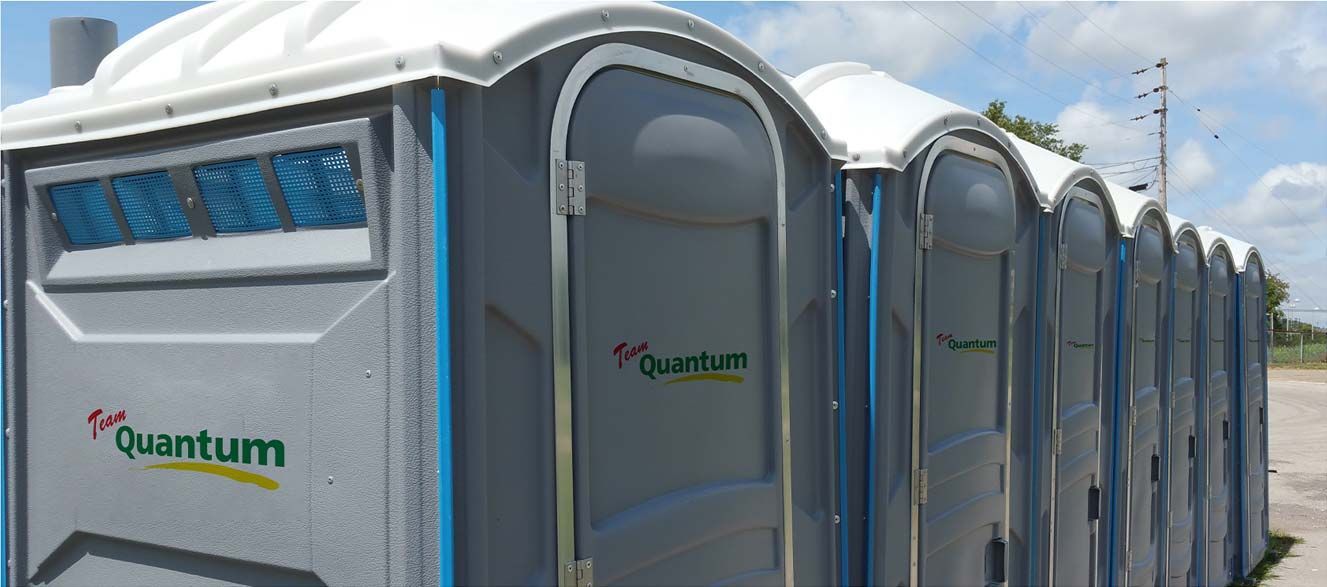 Row of gray portable toilets with blue vents under a cloudy sky