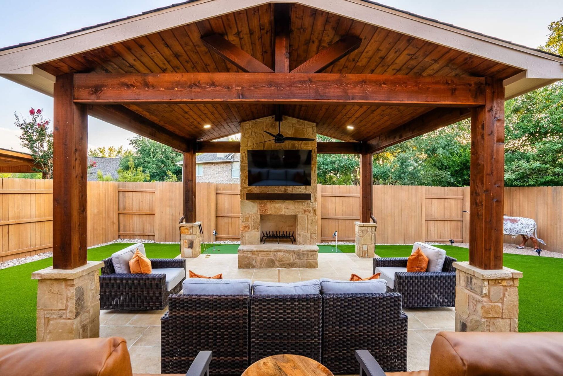 A patio with wicker furniture and a fireplace under a wooden gazebo