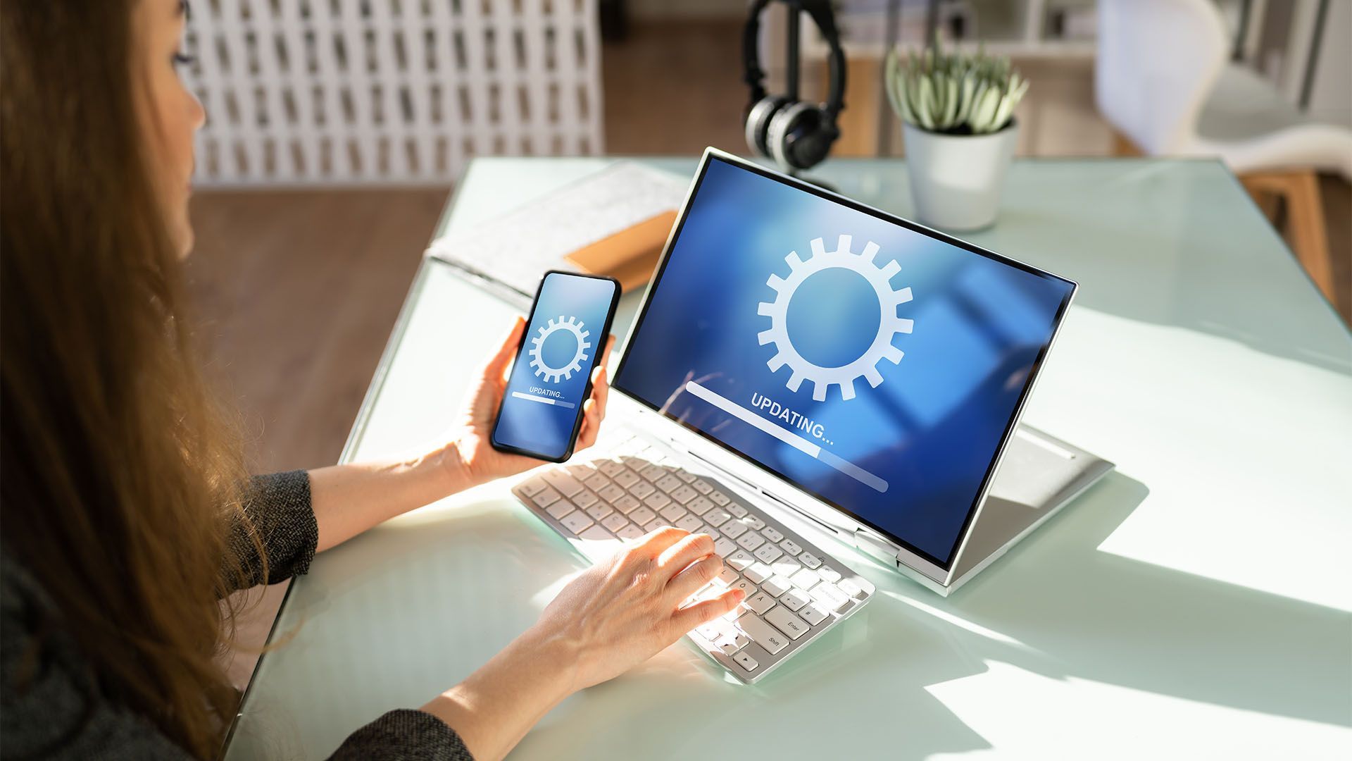 Mulher atualizando o software do laptop e do celular. Ambas as telas exibem um ícone de engrenagem com uma barra de progresso.