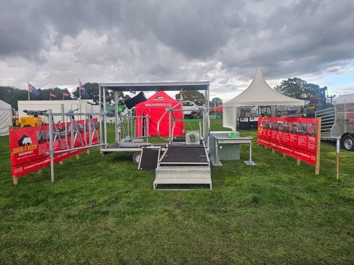 A mobile livestock handling station and red banners on a grassy field under a cloudy sky.