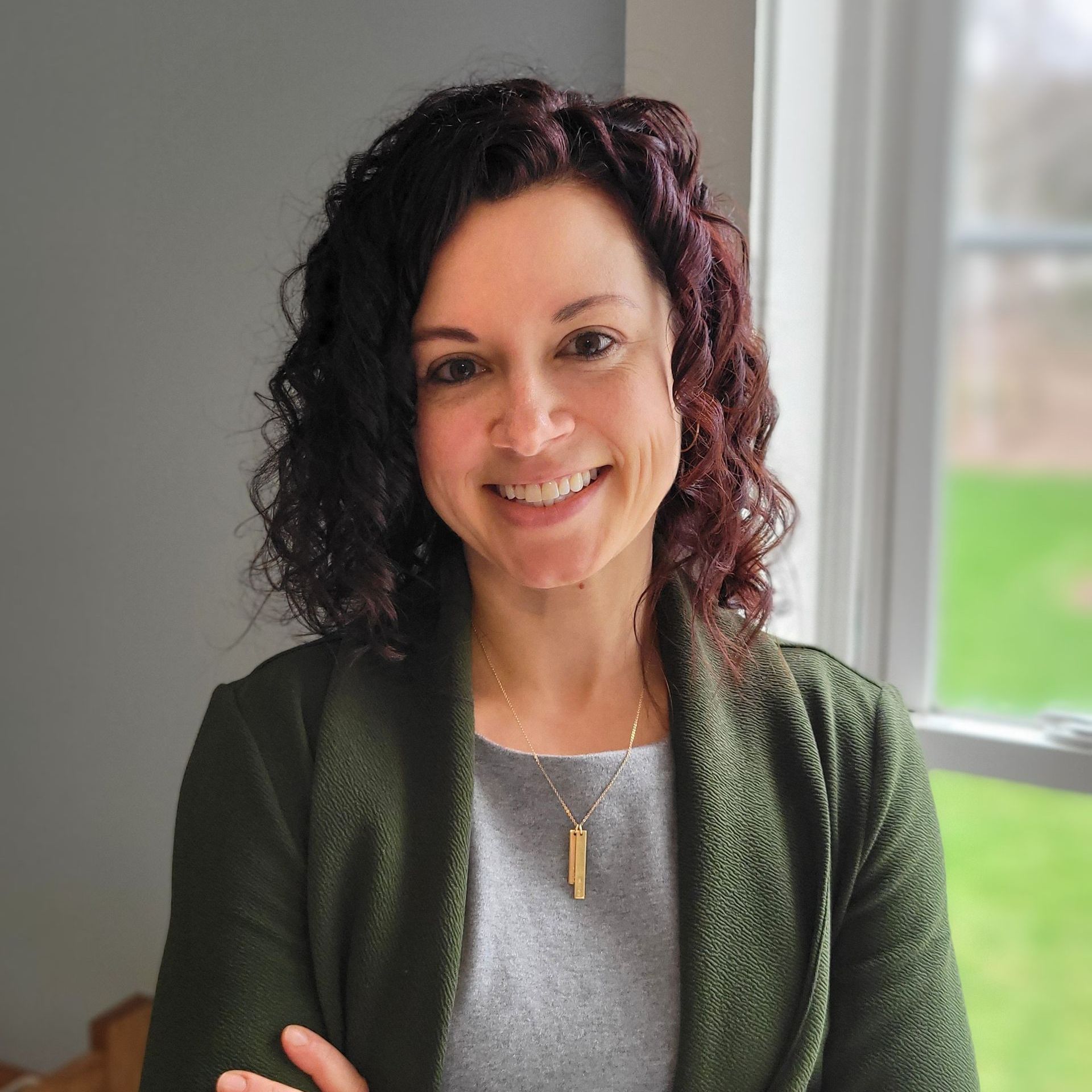 A woman in a green jacket is smiling in front of a window