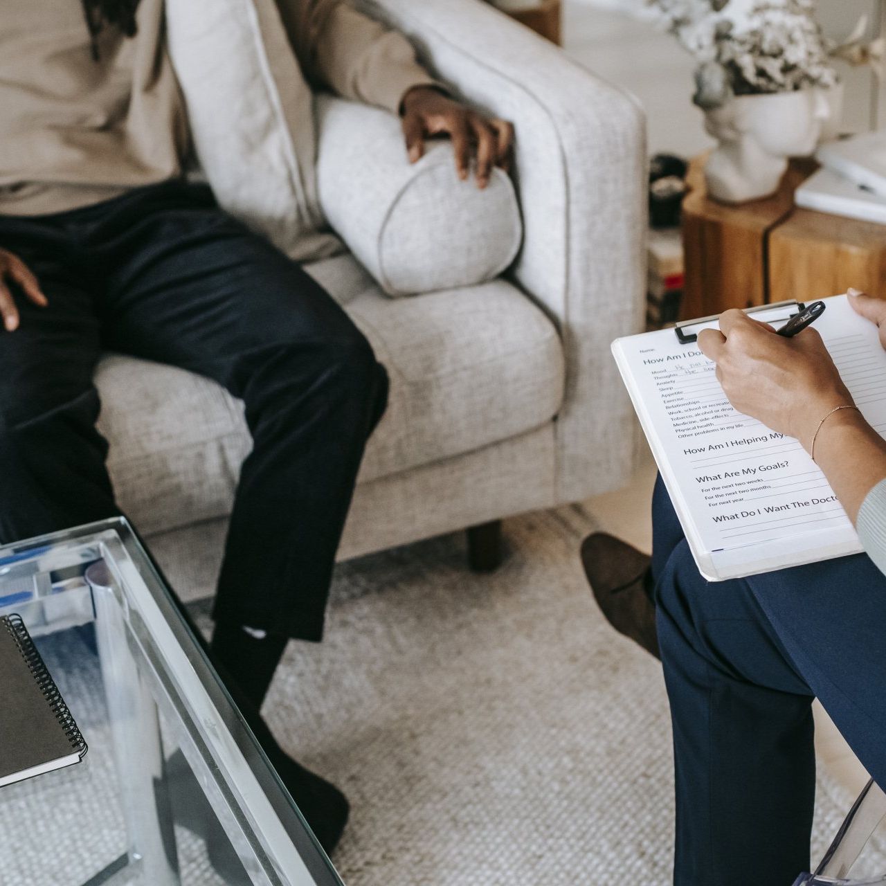 A woman is writing on a clipboard while a man sits on a couch.
