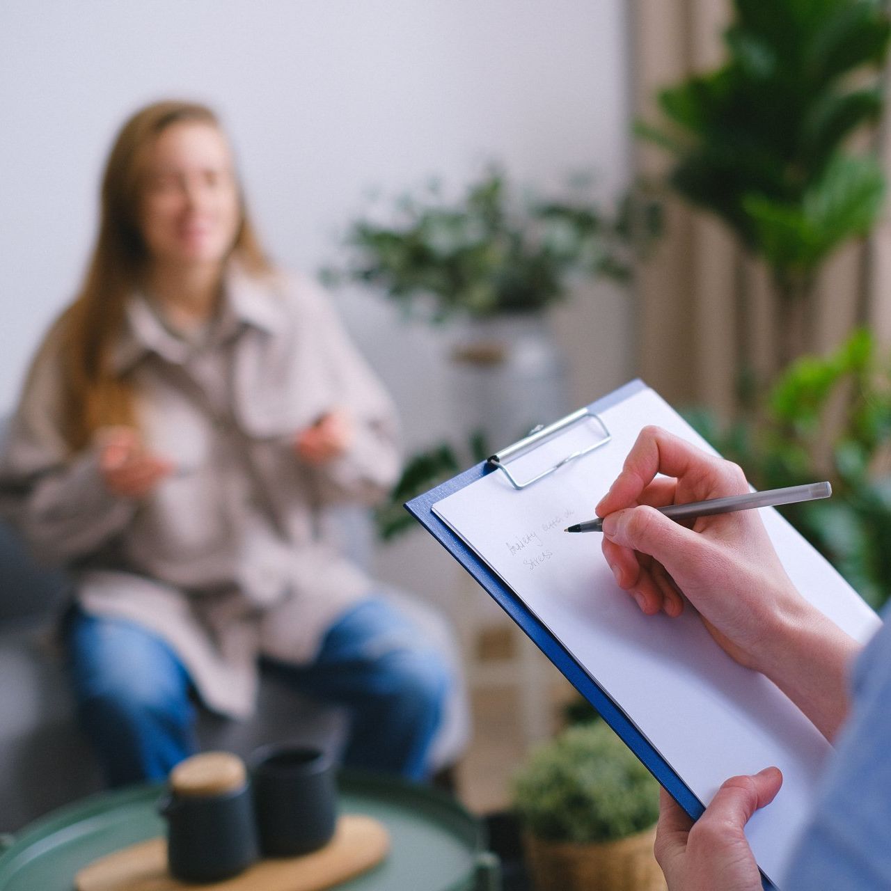 A woman is sitting on a couch while a person writes on a clipboard.