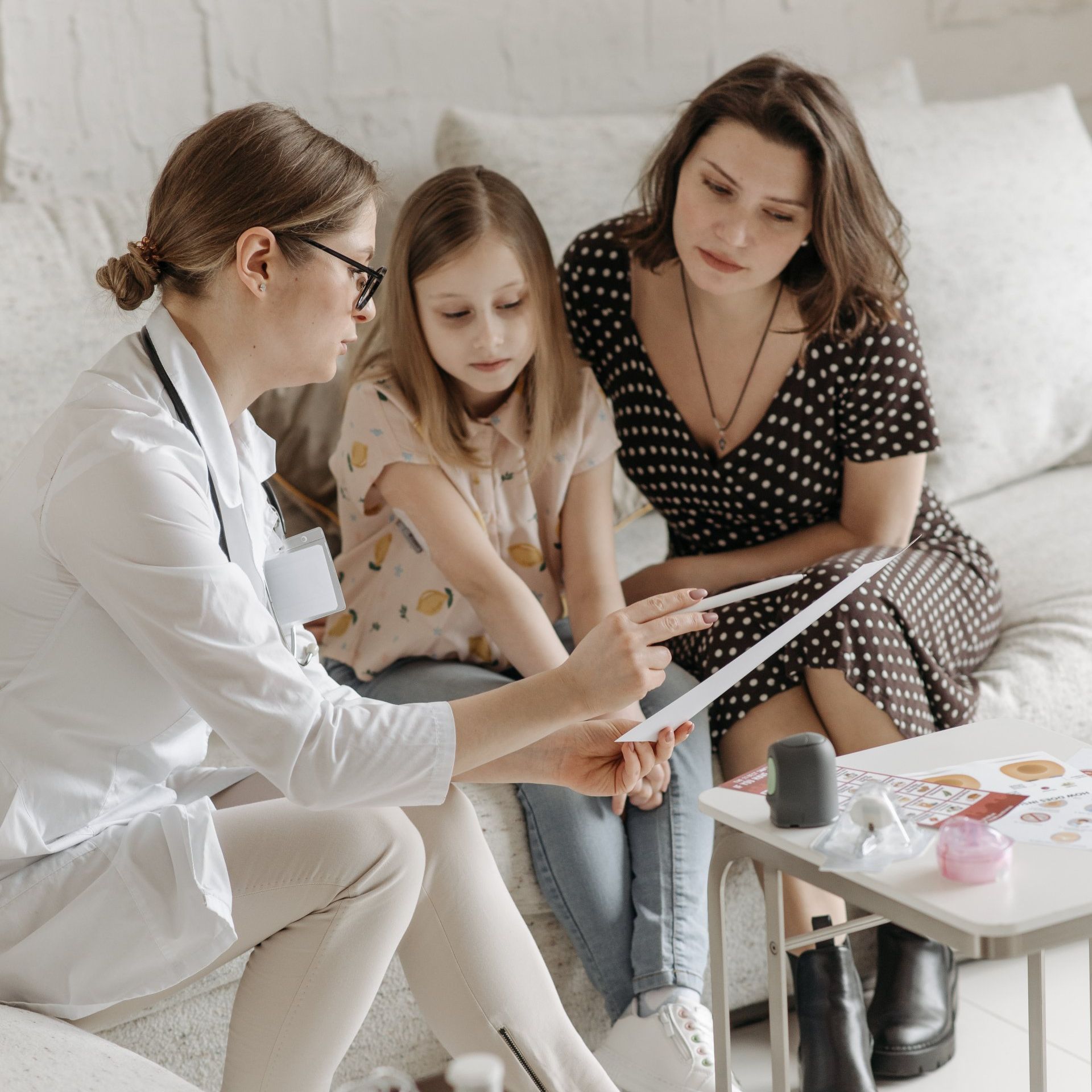 A doctor is talking to two women and a little girl while sitting on a couch.