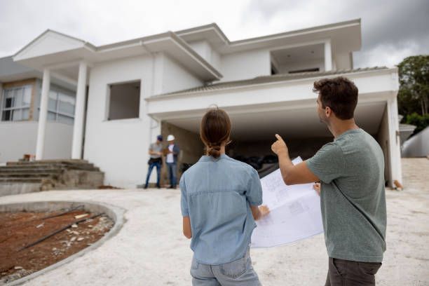 A man and a woman are looking at a blueprint of a house under construction.