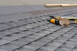 A roof with shingles being installed and tools on it.