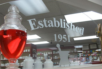 Red liquid in a bottle in a pharmacy, with “Established 1951” on the wall behind it.