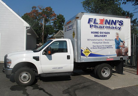 White delivery truck for “Flinn’s Pharmacy” parked outdoors beside a house.