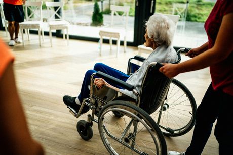 Person being pushed in a wheelchair indoors by another person in a red shirt