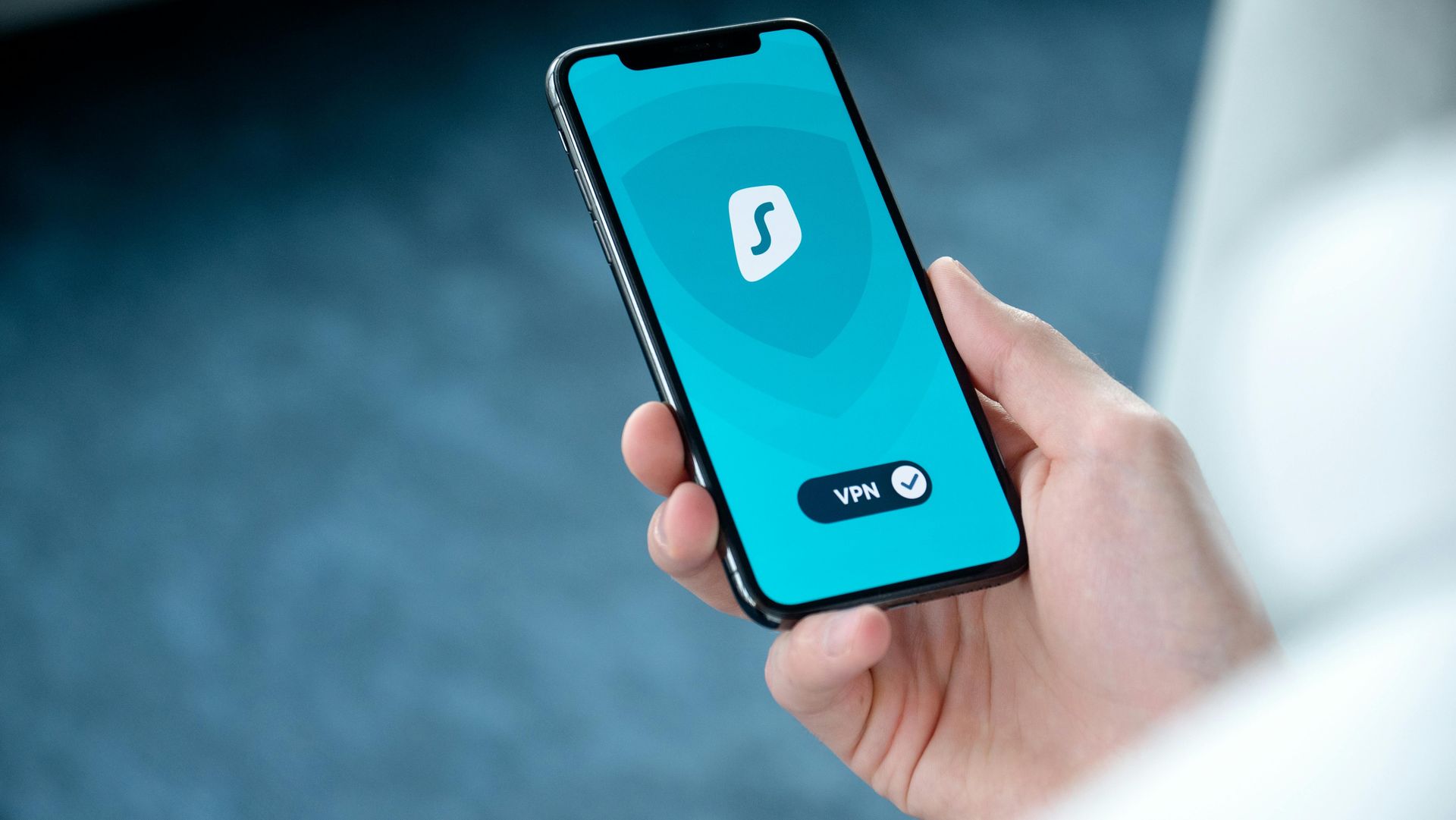 Hand holding a smartphone with a blue app screen and white logo