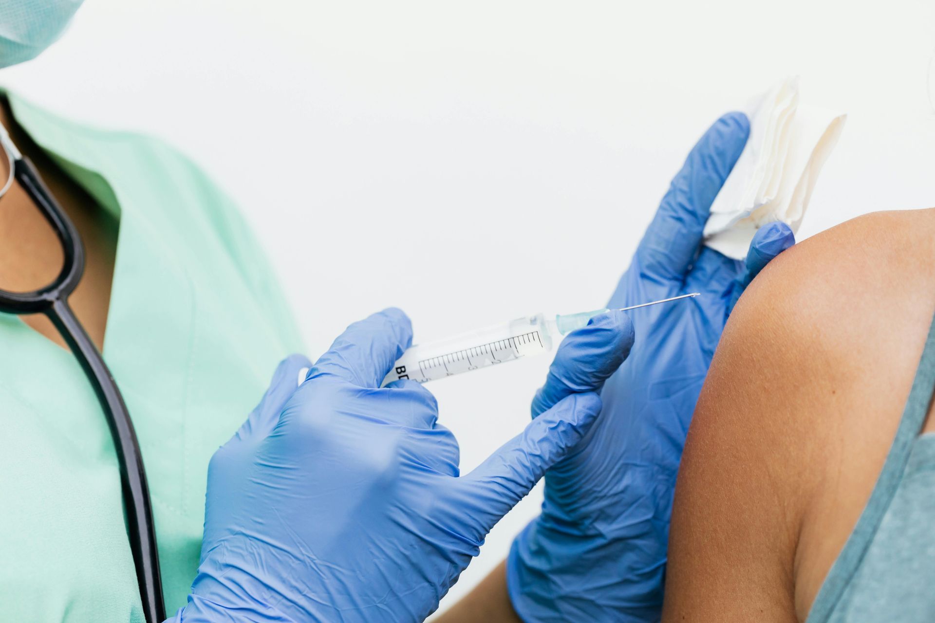 Healthcare worker giving a vaccine injection into a patient’s upper arm, with blue gloves and a syringe