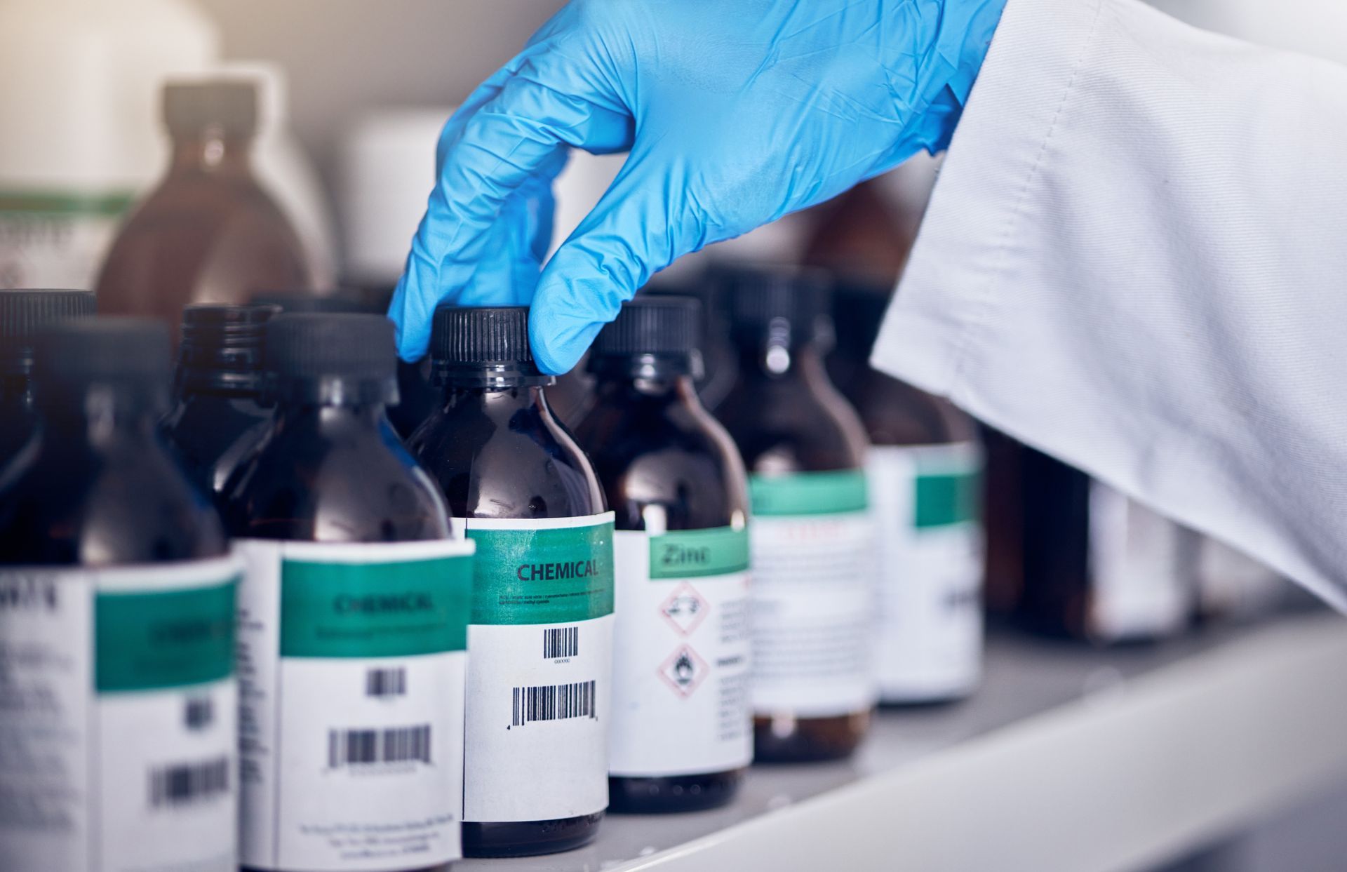 Gloved hand reaching for labeled medicine bottles on a laboratory shelf