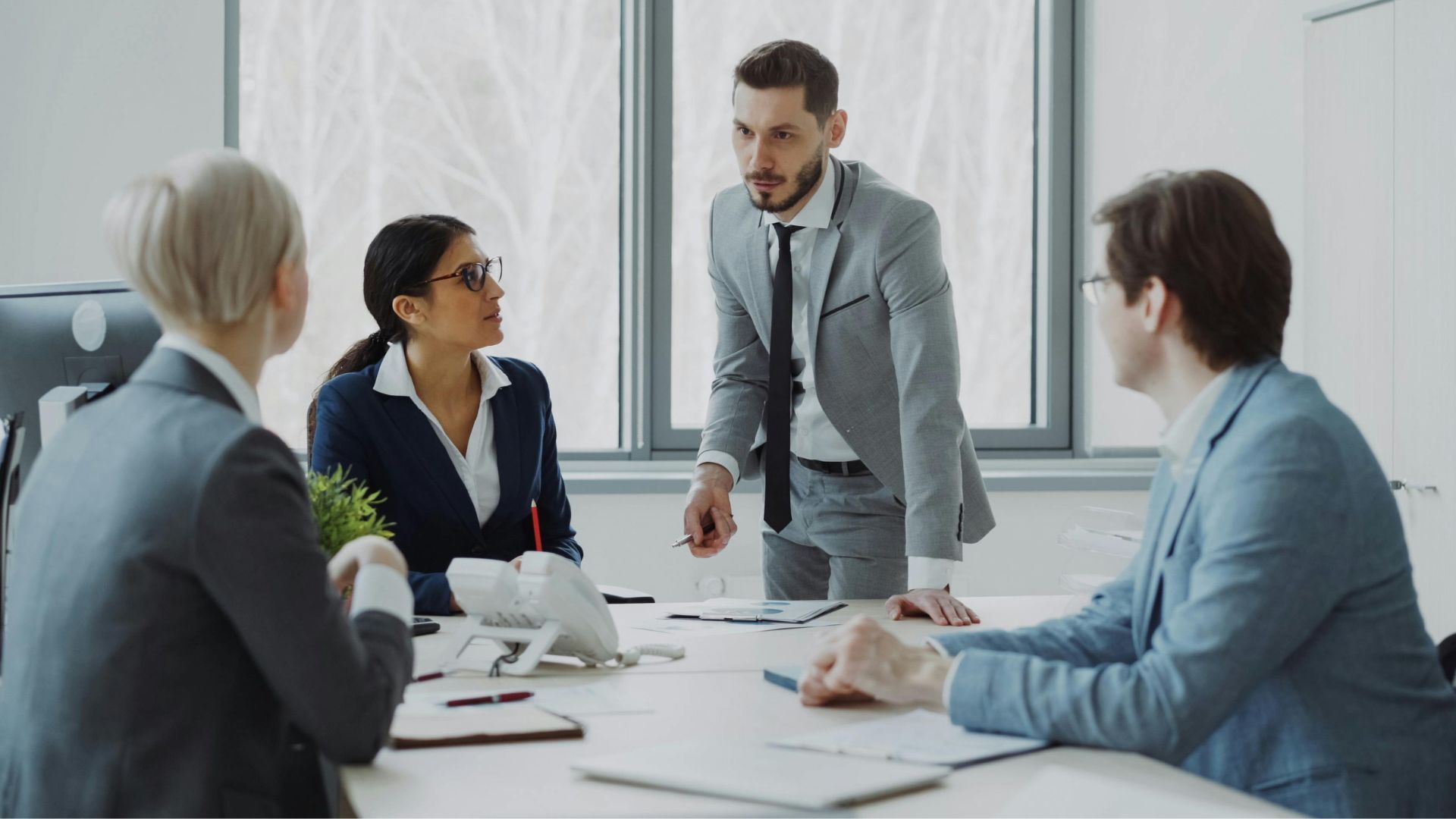 Four coworkers in a meeting, discussing documents around a table in a bright office.