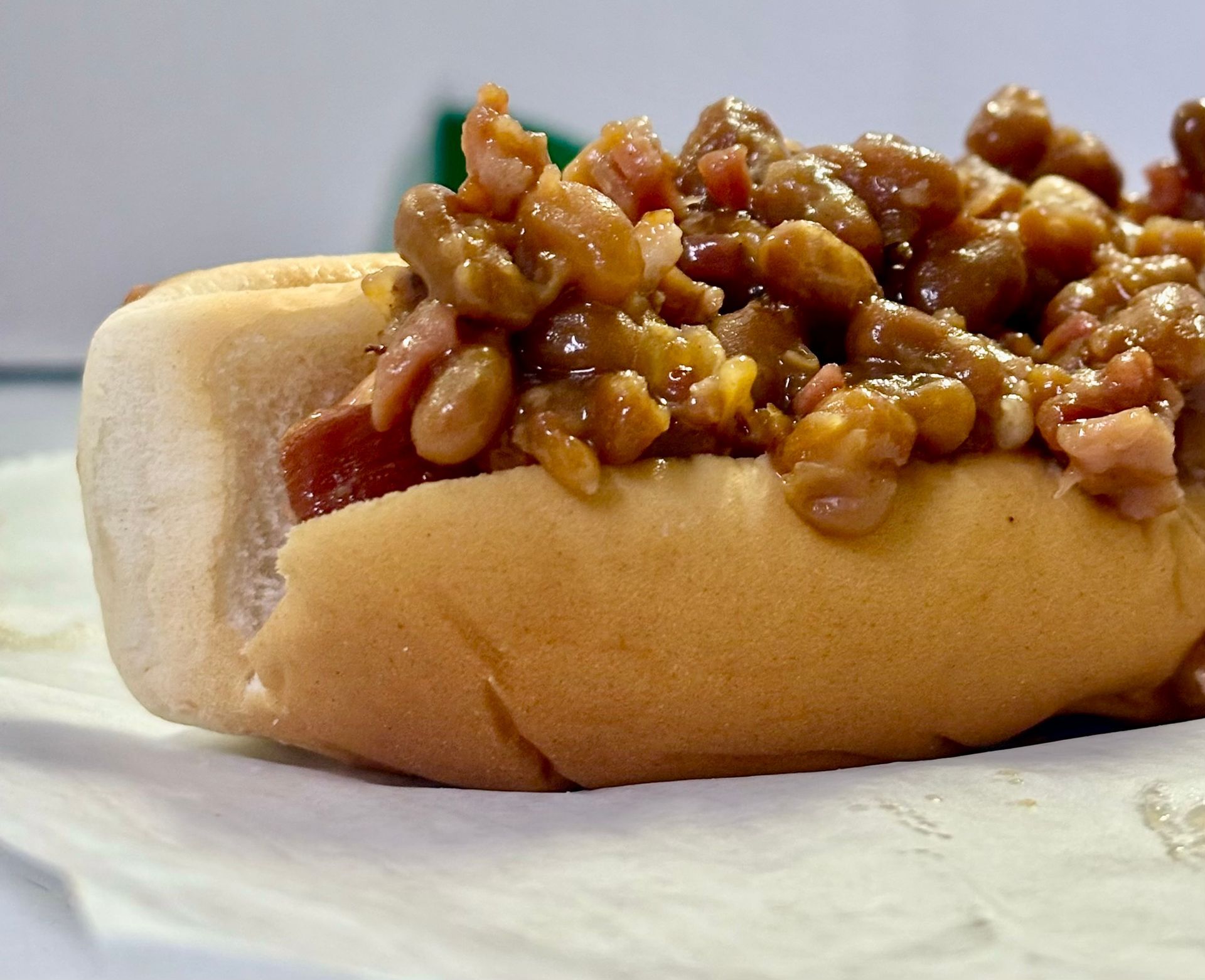 Hot dog in a bun, topped with baked beans and chopped bacon.