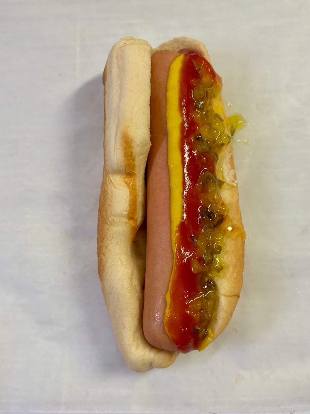 Hot dog in a bun, topped with yellow mustard, ketchup, and relish.