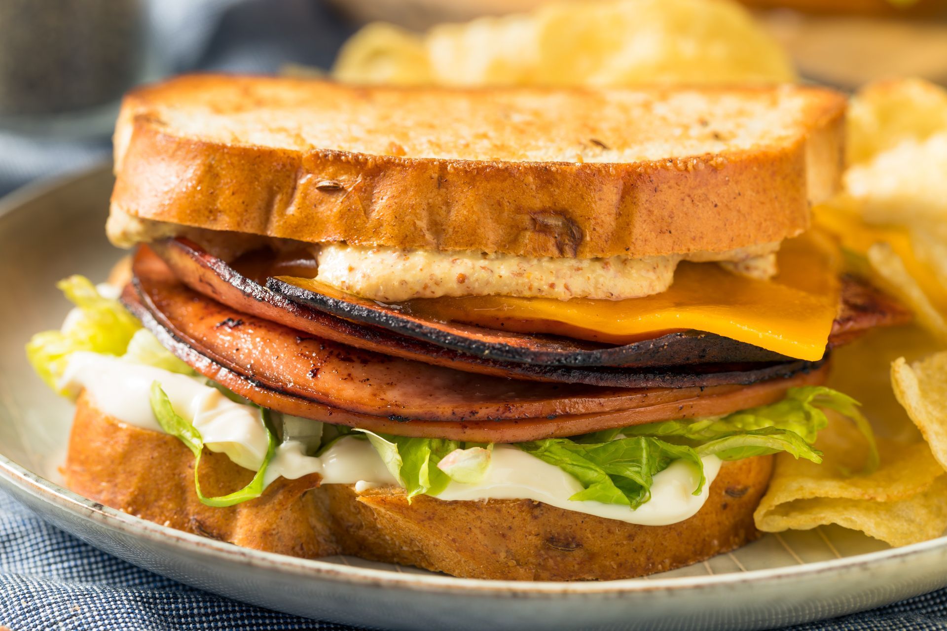 Bologna sandwich on toasted bread with lettuce, cheese, and chips on a plate.