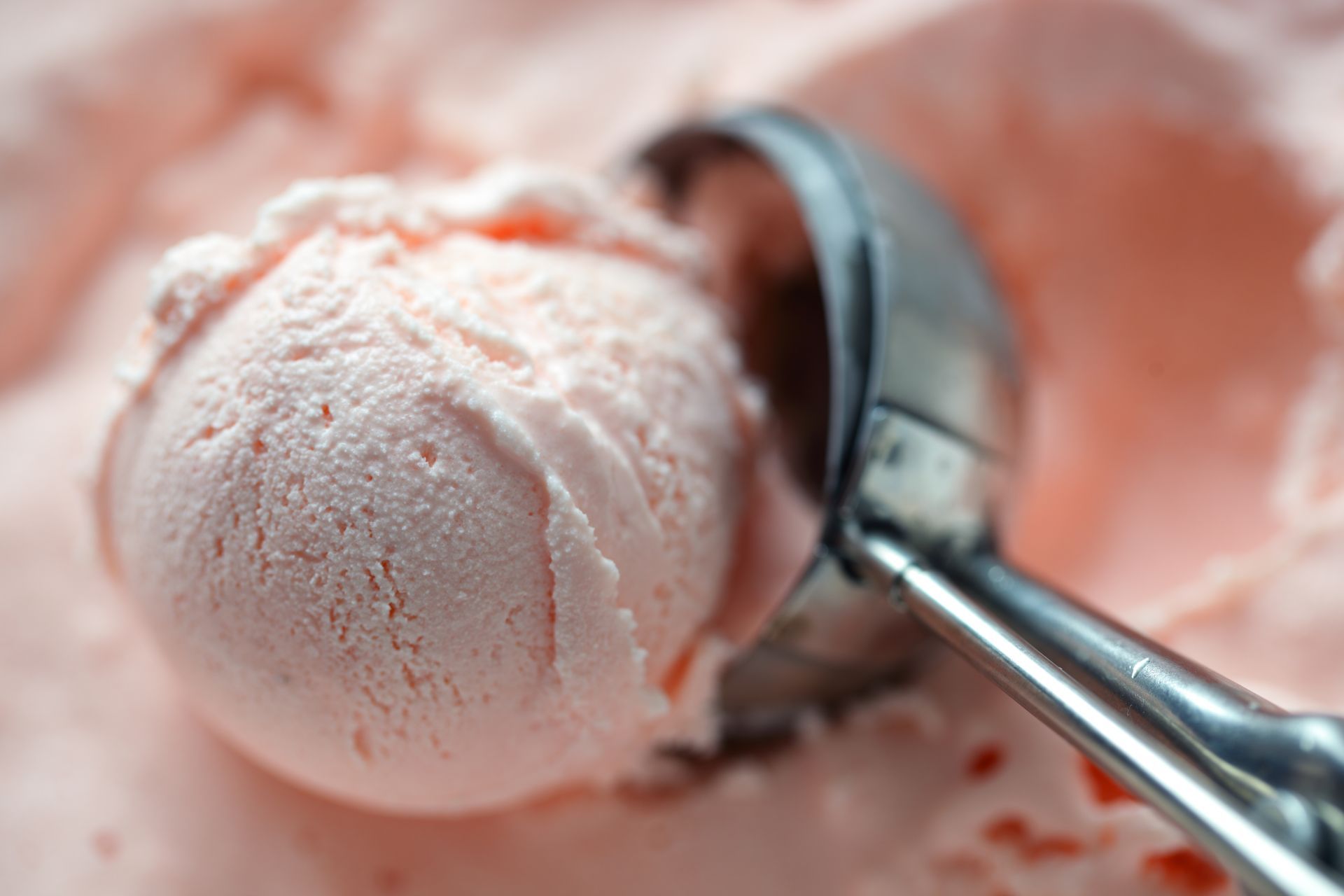Pink ice cream scoop in a container, with a round scoop held by a silver scoop.