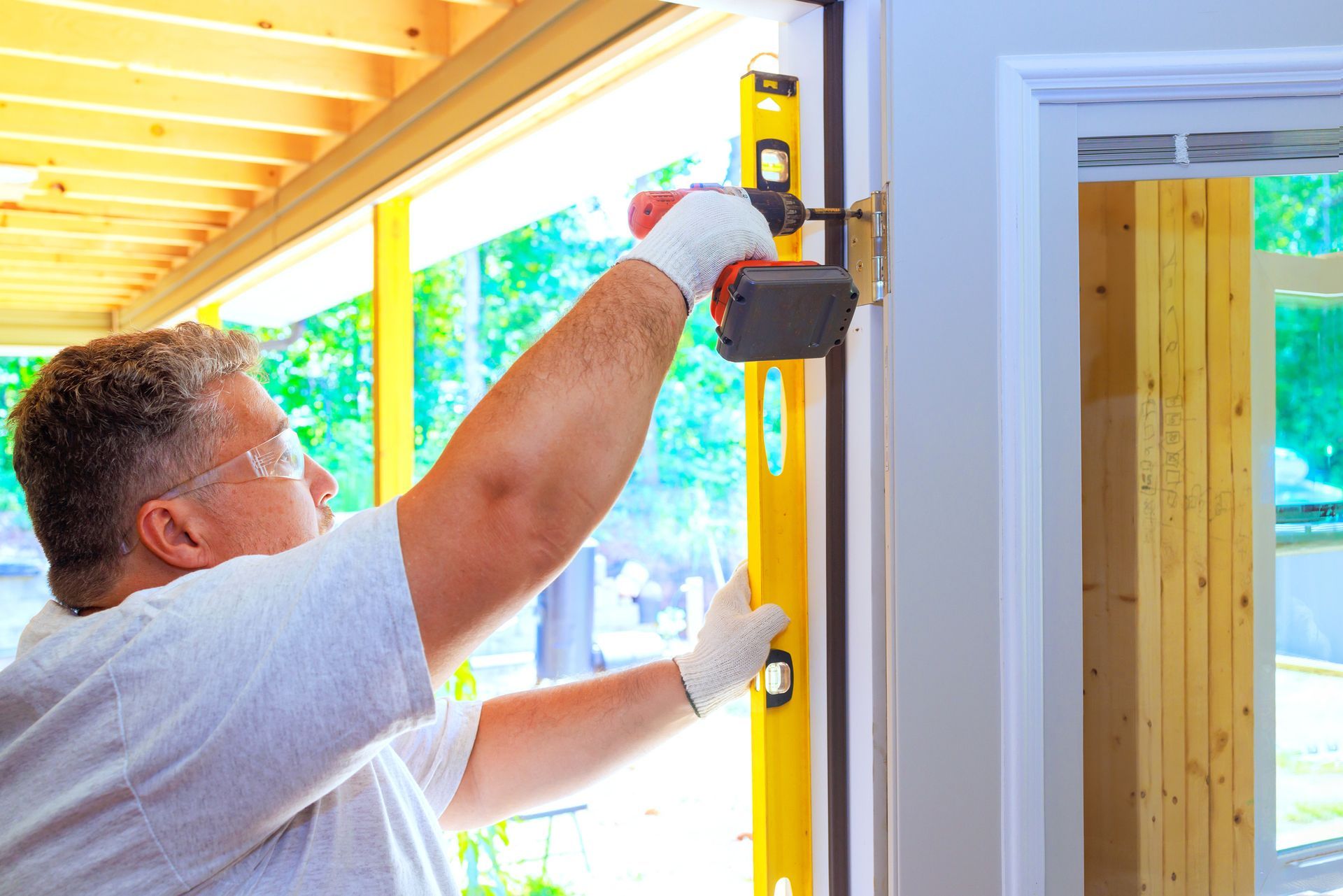 A man is using a drill and a level to install a door.