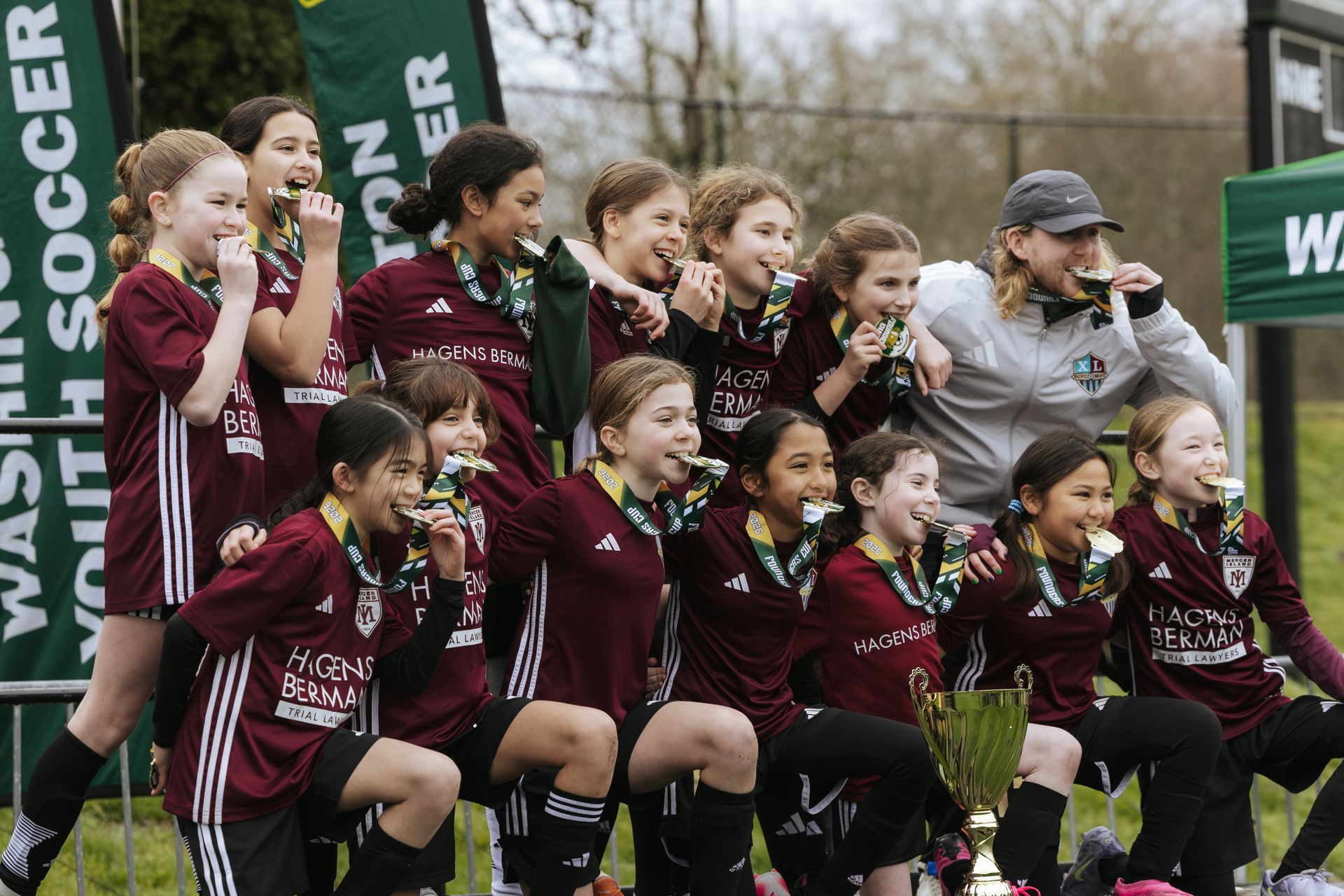Youth soccer team in maroon uniforms posing with a coach on the field, cheering before a game.