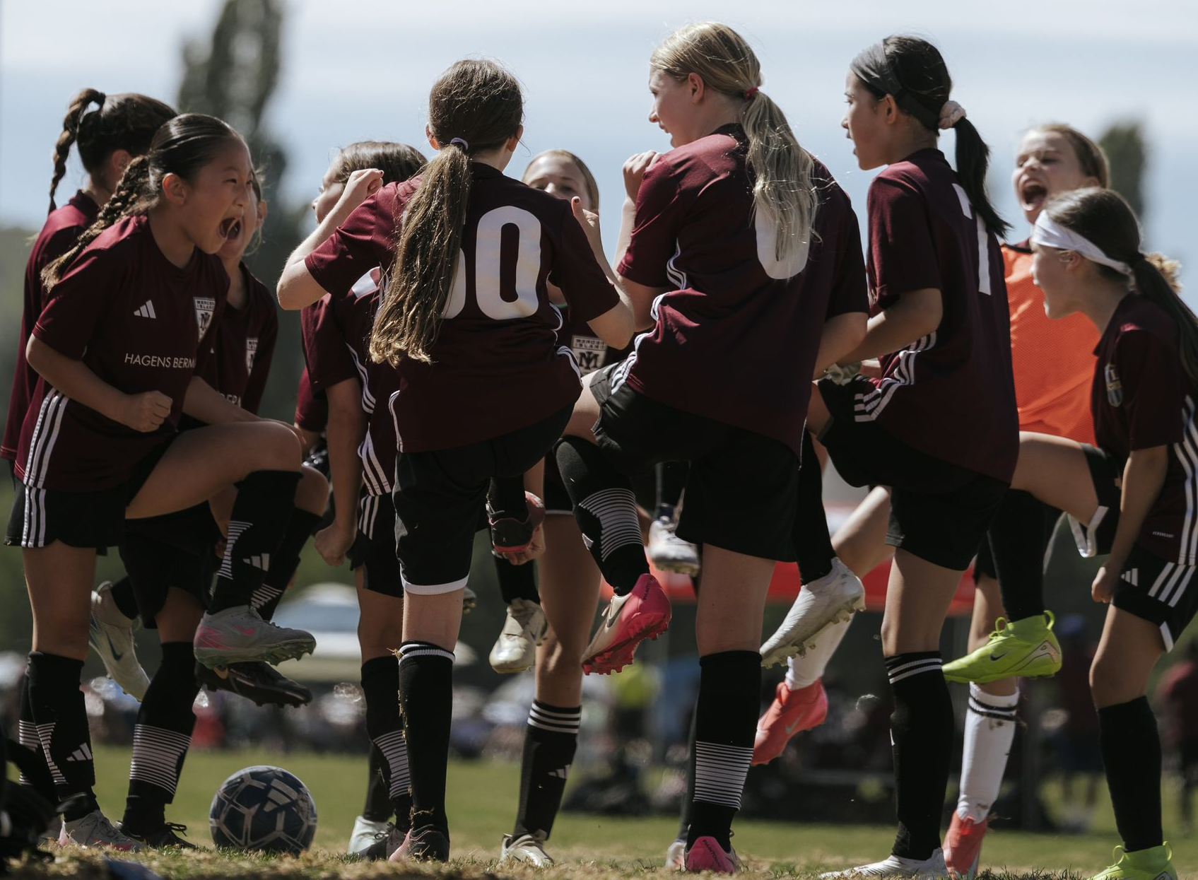 Soccer players in maroon jerseys huddle on a sunny field during a game