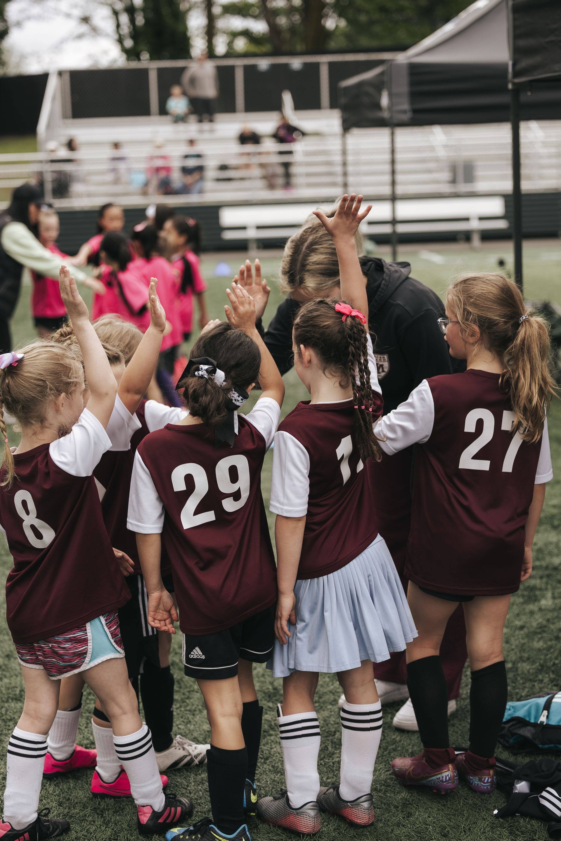 Youth soccer team in maroon jerseys huddles and raises hands on the field after a game.