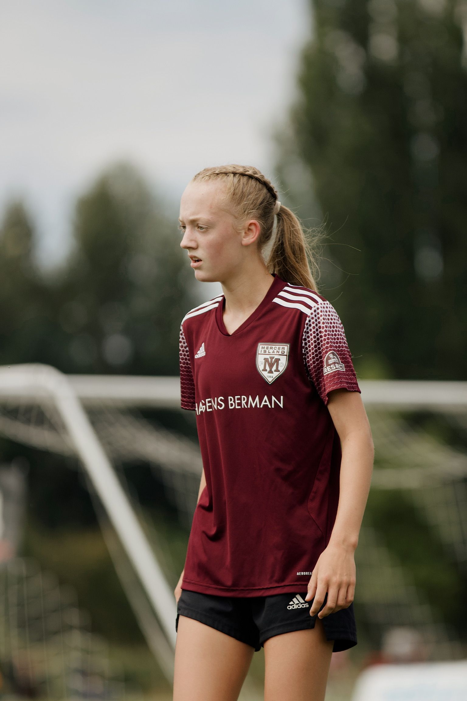 Soccer player in maroon jersey walking on a field, looking to the side.