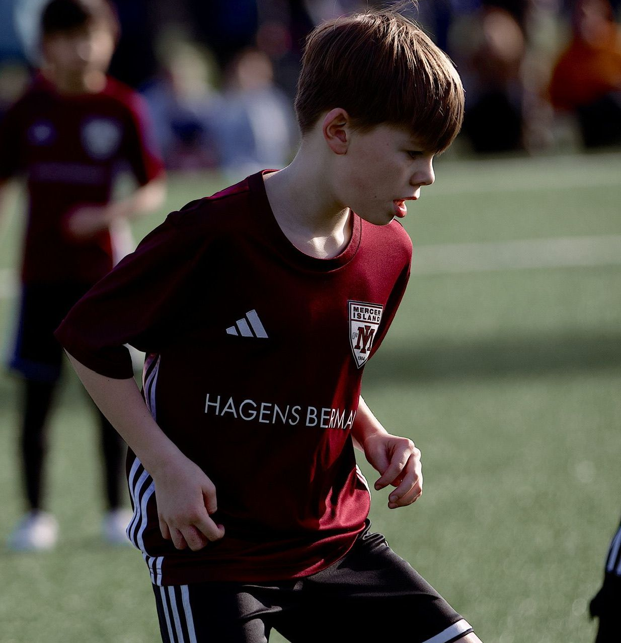 Young soccer player in a maroon jersey running on a field during a match