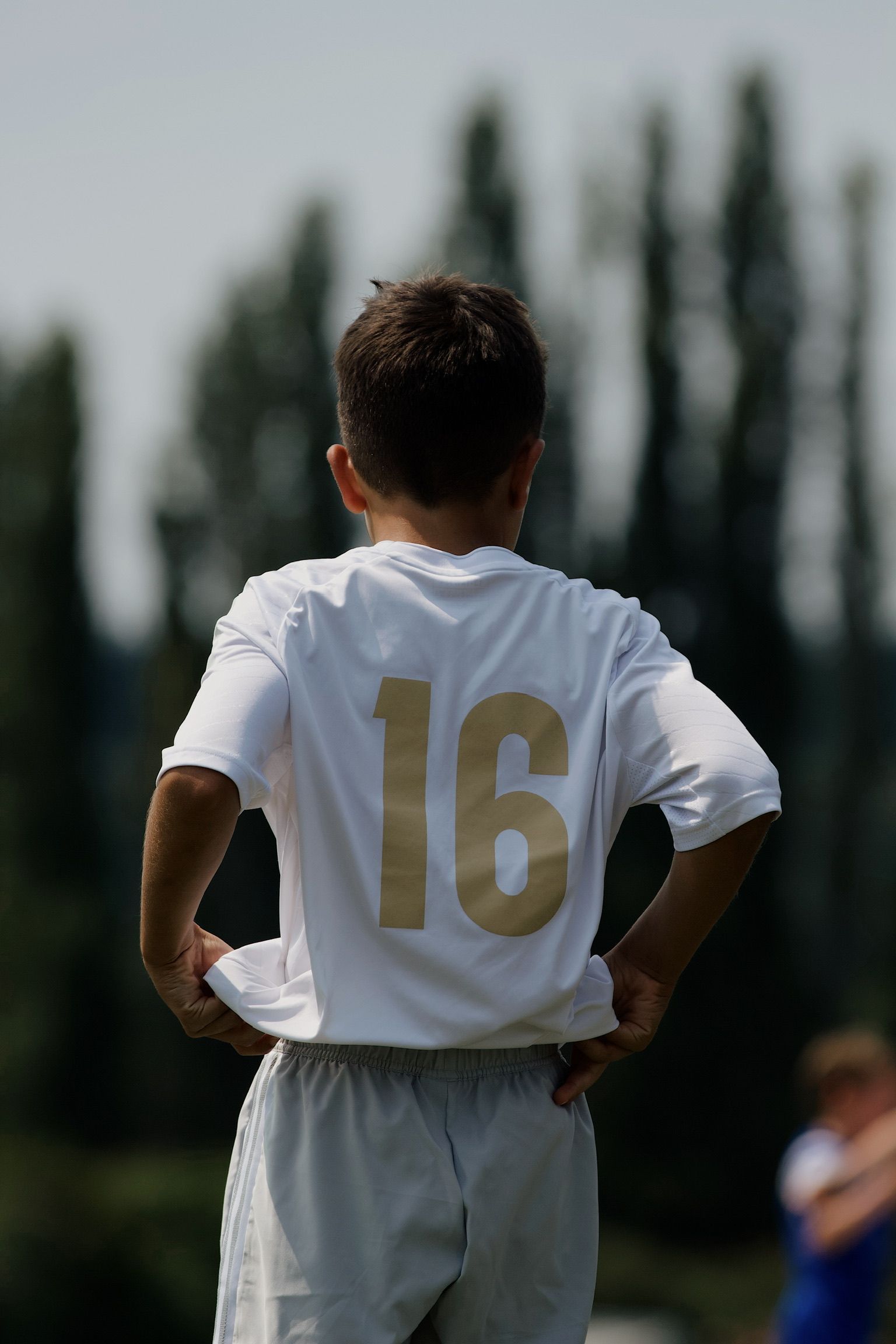 Soccer player in white jersey number 16 stands with hands on hips on a field