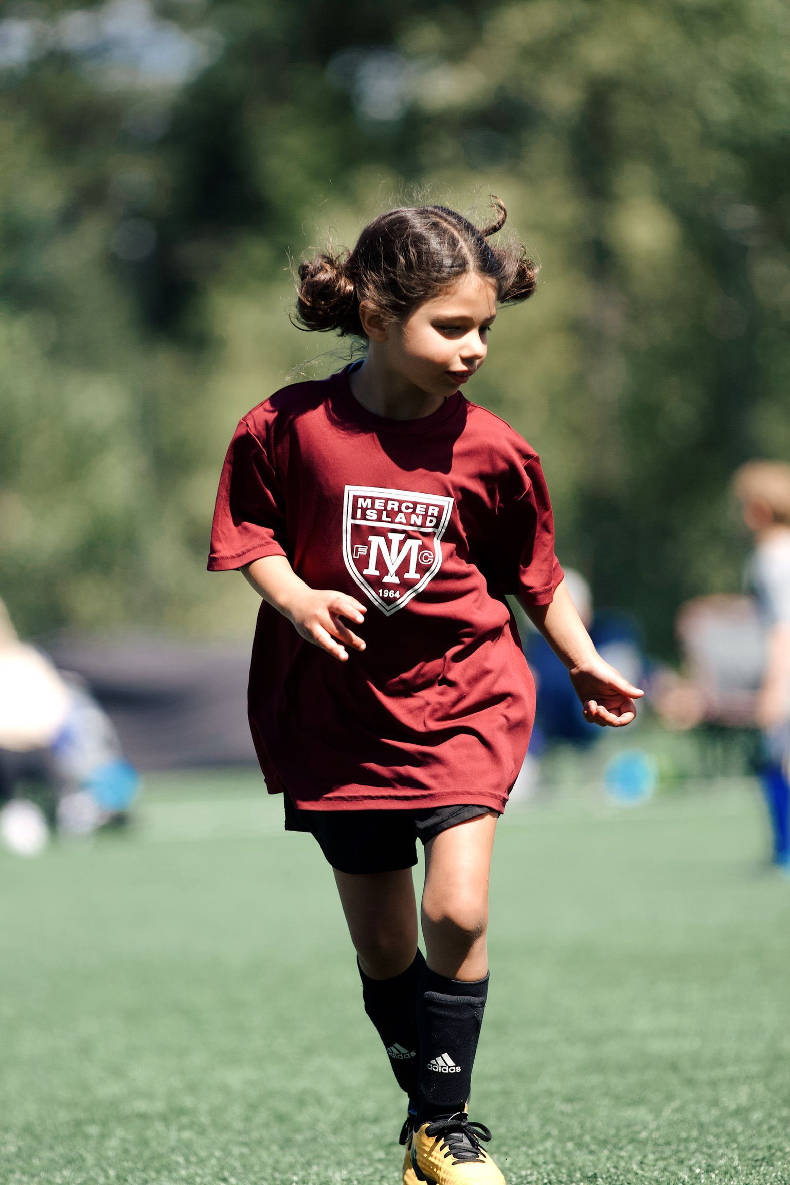 Child in maroon jersey running on a soccer field, with a blurred background.