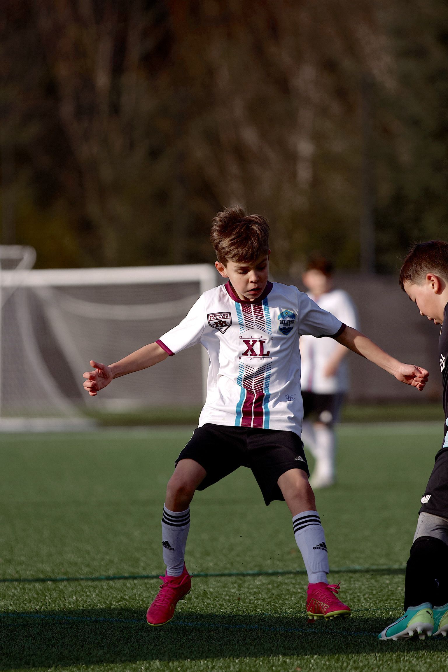 Soccer player in white and black uniform dribbles on a field, flanked by opponents.