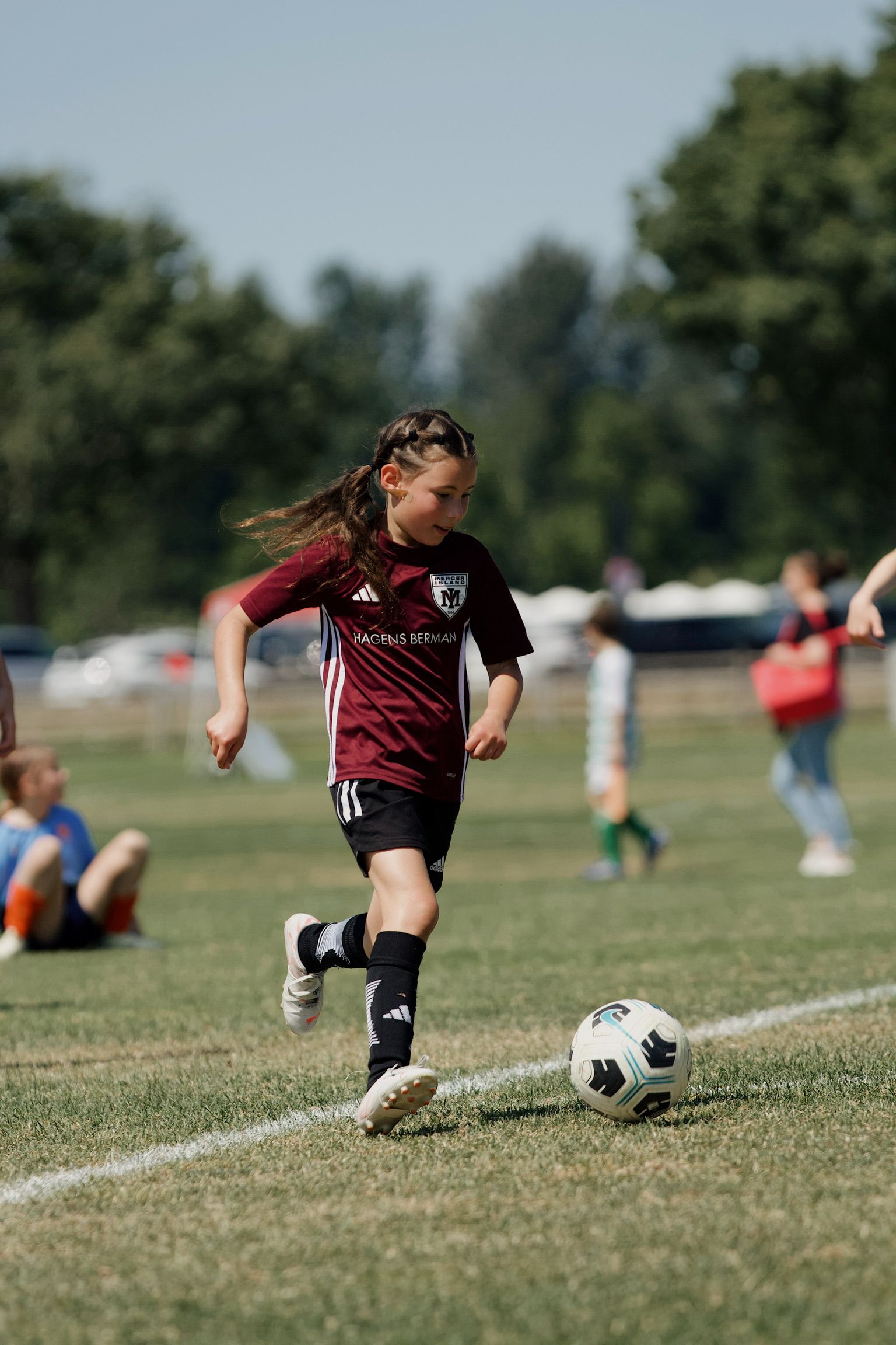 Soccer player in maroon jersey dribbling a ball on a grassy field, with spectators in the background