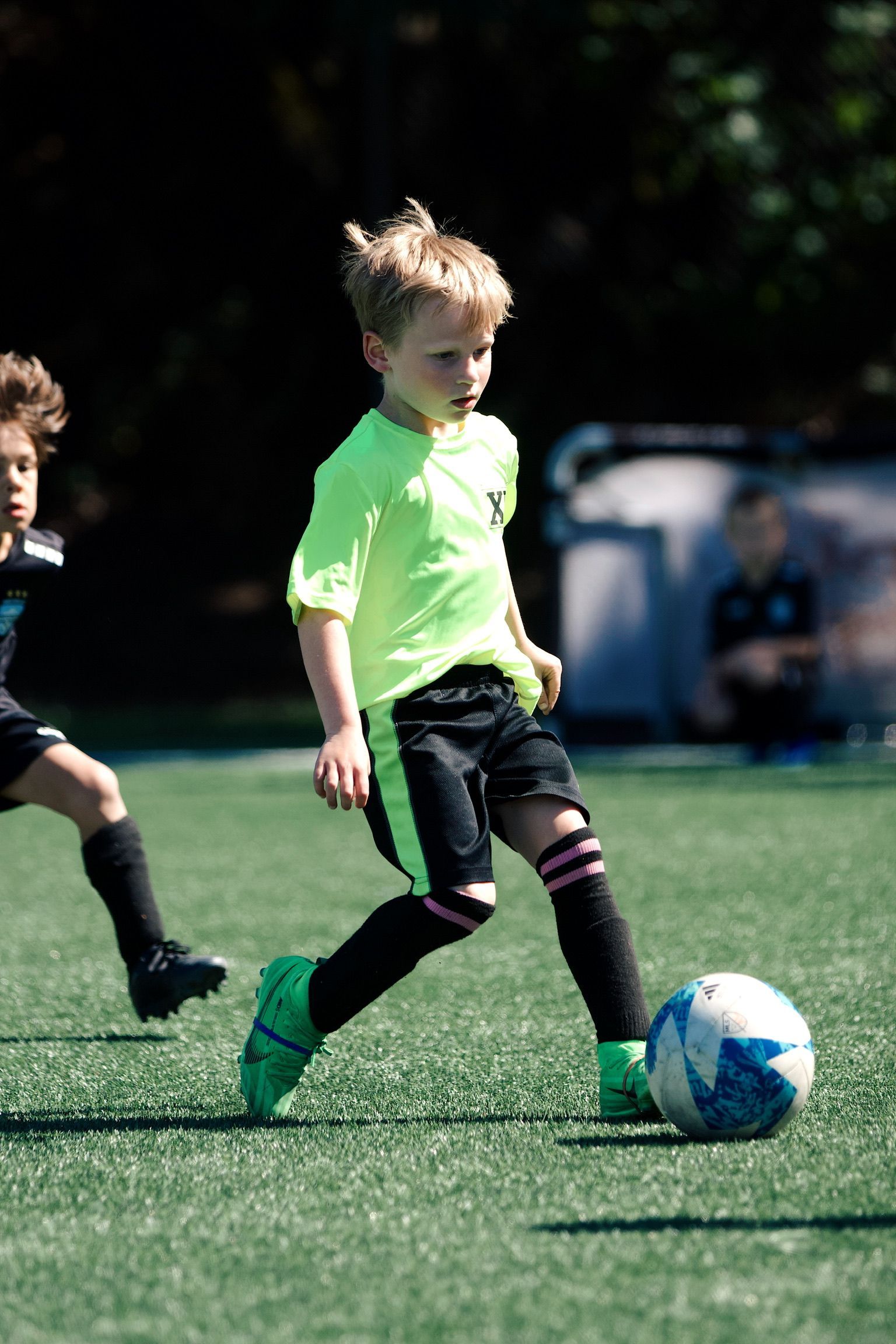 Child in neon green jersey dribbling a soccer ball on a grass field during a game