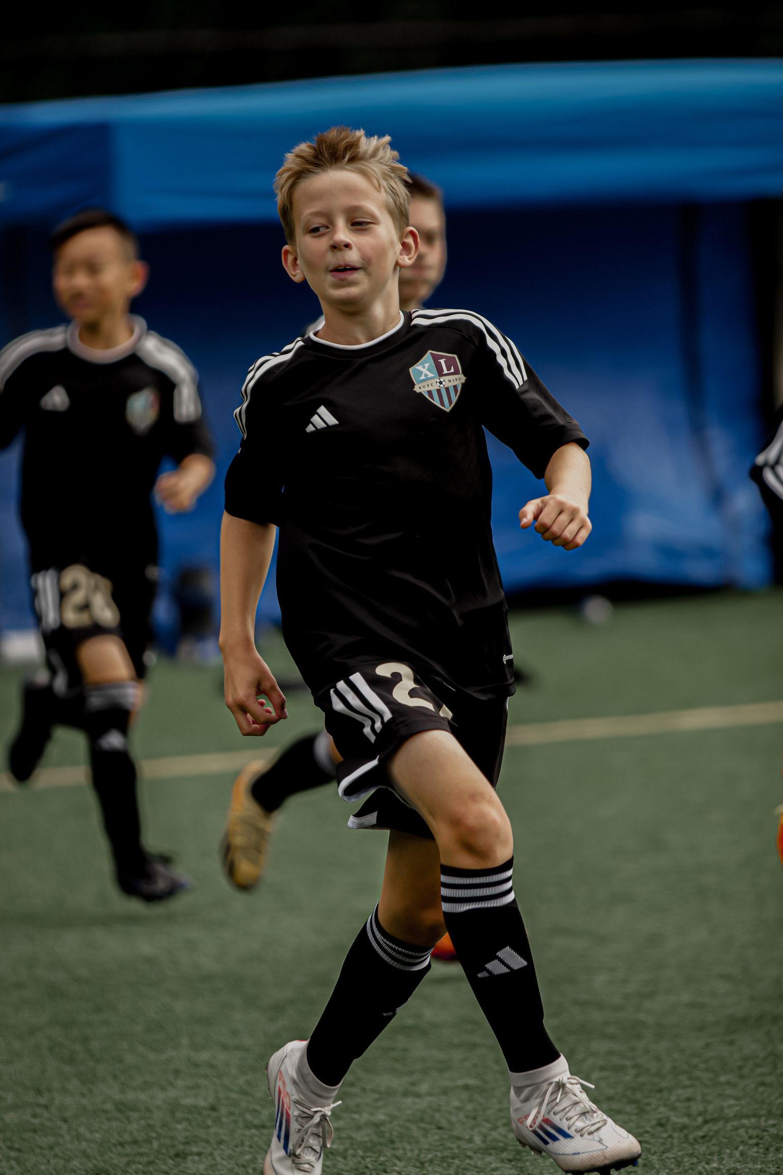 Youth soccer player in black jersey running on indoor field with ball nearby
