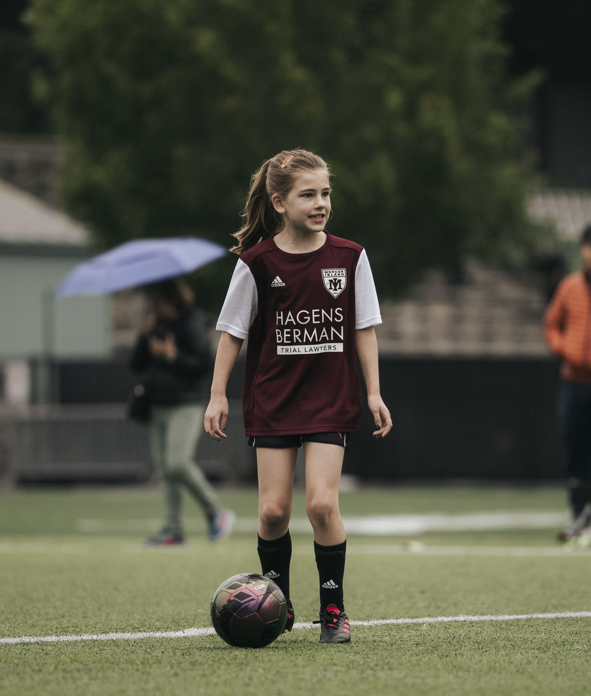 Young soccer player in maroon and white uniform standing by a ball on a field
