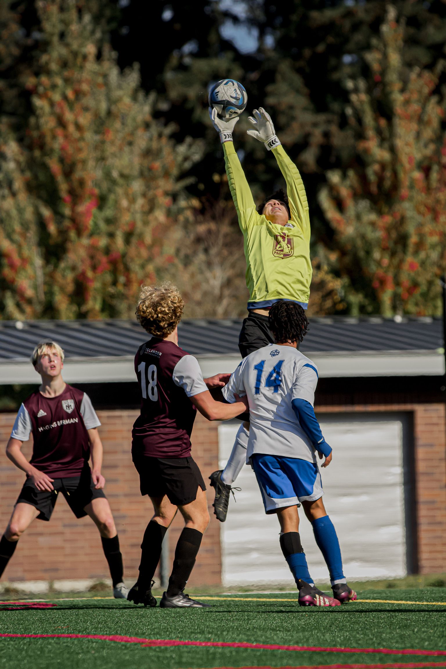 Soccer goalkeeper in lime green jersey leaps to catch a high ball during a match