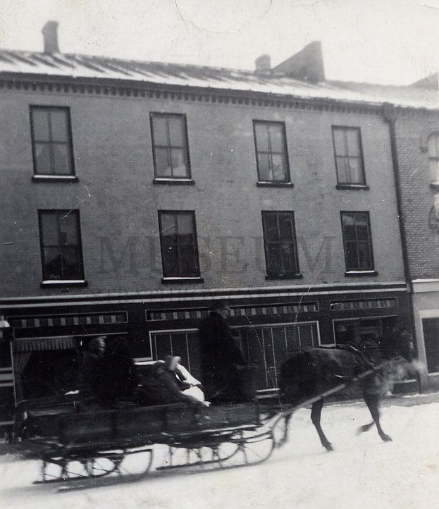 A black and white photo of a horse drawn sleigh in front of a museum
