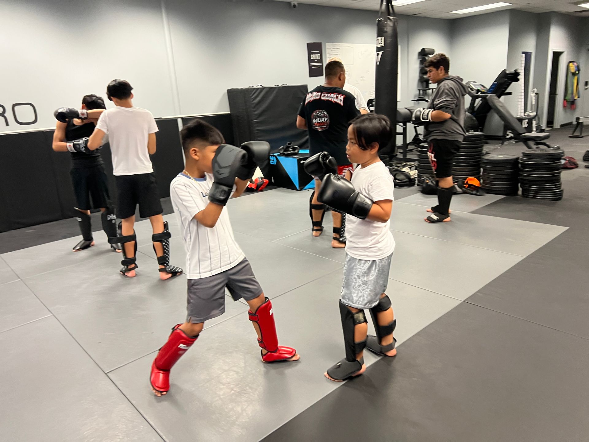 Two kickboxers spar in a boxing ring, one landing a high kick in a dim gym.