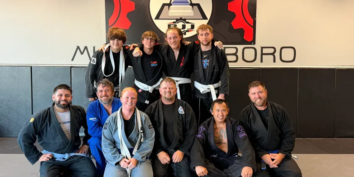 Group portrait of ten people posing indoors in front of a wall with a large Ground Level MMA & Fitness Logo
